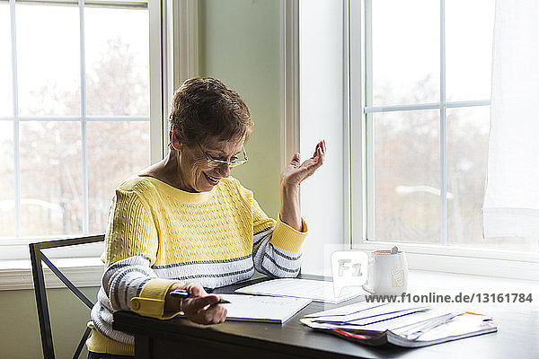 Glückliche ältere Frau schreibt am Schreibtisch