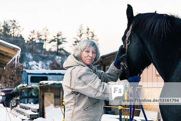 Senior adult woman standing with horse in snowy landscape