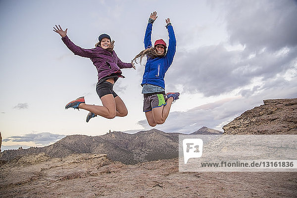 Two young female climbers jumping mid air on top of Smith Rock  Oregon  USA