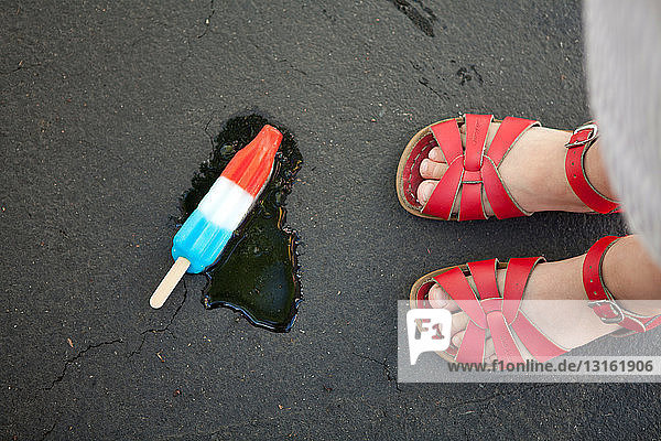 Mädchen in roten Sandalen mit Eis am Boden