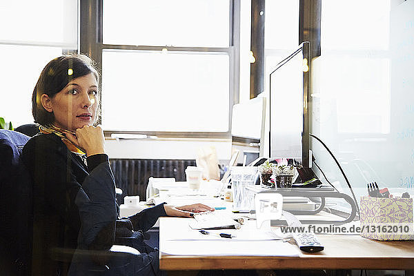 Geschäftsfrau am Schreibtisch mit Hand am Kinn