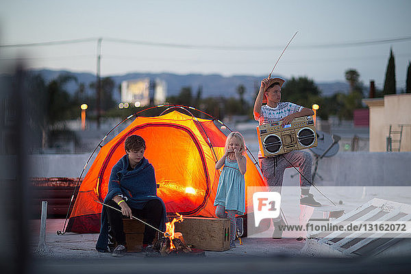 Teenager-Jungen mit Schwester und Boombox neben orangefarbenem Zelt auf dem Dach