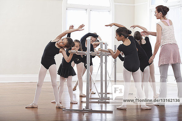 Ballettlehrerin unterrichtet Gruppe von Mädchen Ballettposition an der Stange