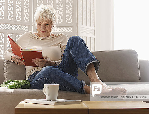 Ältere Frau entspannt sich auf Sofa mit Buch