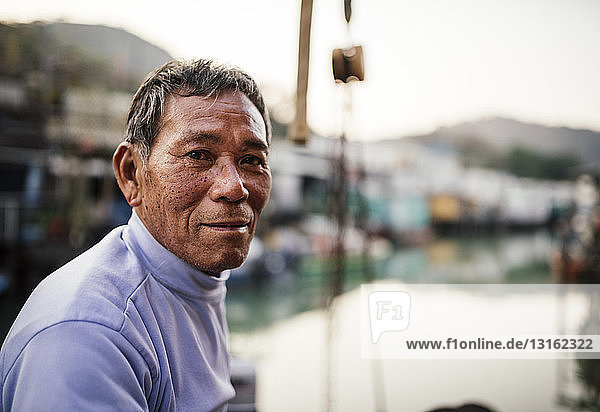 Porträt eines älteren Mannes  Seitenansicht  vor Booten auf dem Wasser  in die Kamera blickend