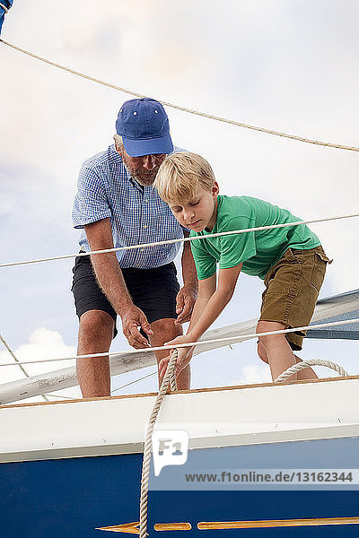 Junge hilft Großvater beim Ziehen von Seilen auf Segelboot