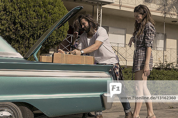 Young couple packing vintage car boot for road trip