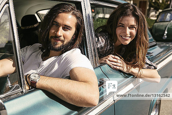 Young couple leaning out of vintage car windows