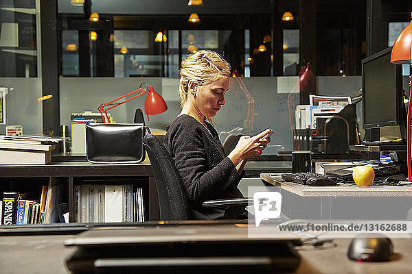 Weibliche Büroangestellte am Schreibtisch mit Mobiltelefon