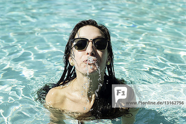 Porträt einer jungen Frau im Schwimmbad  die Wasser aus dem Mund spritzt