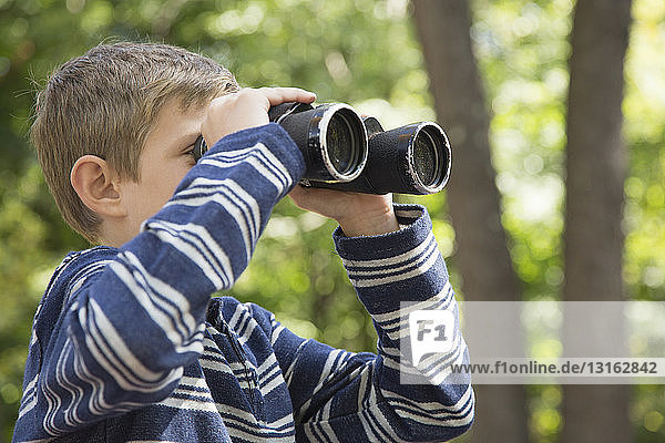 Boy looking through binoculars in woods