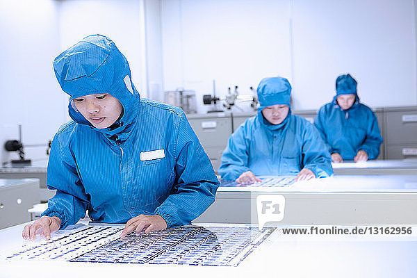 Arbeiterinnen inspizieren flexible Schaltungen im Reinraum einer flexiblen Elektronikfabrik
