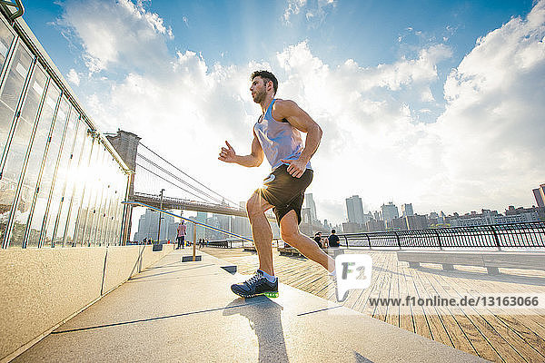 Young male runner running up riverside stairs  New York  USA