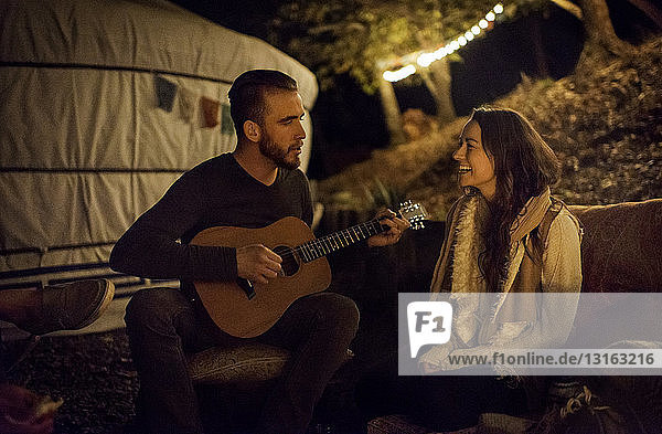 Young man serenading young woman with guitar next to yurt