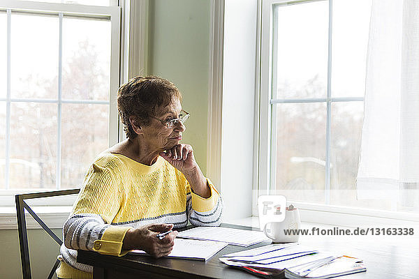 Ältere Frau denkt am Schreibtisch