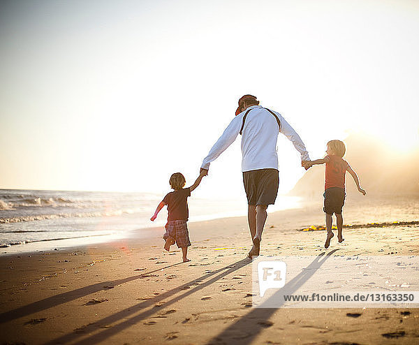 Vater und Söhne gehen bei Sonnenuntergang Hand in Hand am Strand