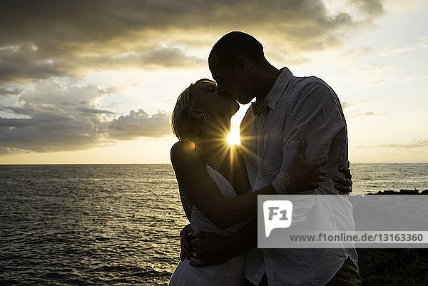 Ein Paar küsst sich bei Sonnenuntergang am Meer