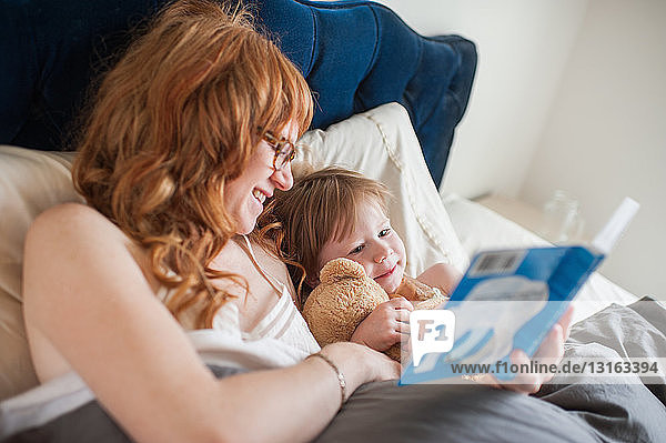 Mutter und Tochter lesen Buch im Bett liegend