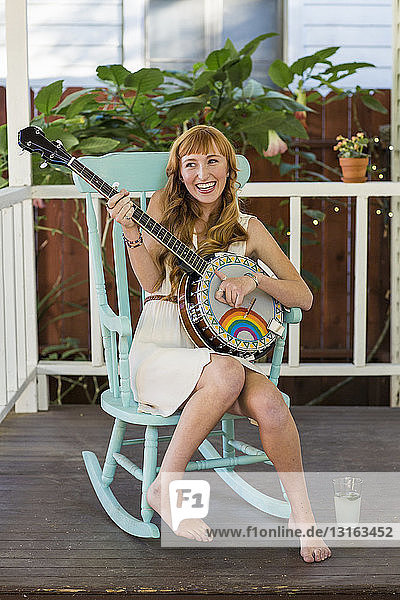 Junge Frau sitzt auf Schaukelstuhl und spielt Banjo
