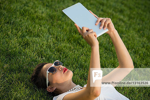 Mittelgroße erwachsene Frauen liegen im Park und verwenden ein digitales Tablett