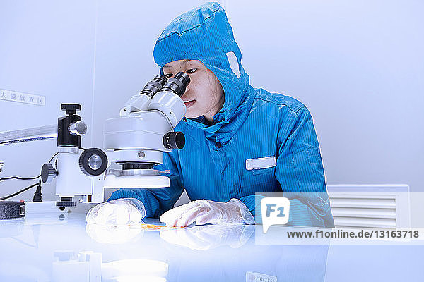 Arbeitnehmerin benutzt Mikroskop zur Untersuchung von flexiblen Schaltkreisen im Reinraum einer flexiblen Elektronikfabrik