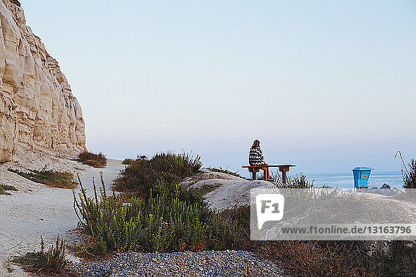 Young woman sitting on clifftop bench looking out to sea  San Clemente  California  USA