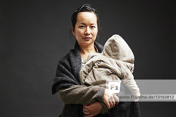 Studioporträt einer mittleren erwachsenen Frau  die einen kleinen Sohn hält