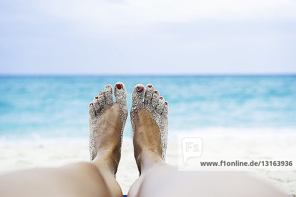 Nahaufnahme der weiblichen Beine und Füße beim Sonnenbaden am Strand