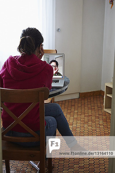 Frau benutzt Laptop für Videoanruf am Esstisch