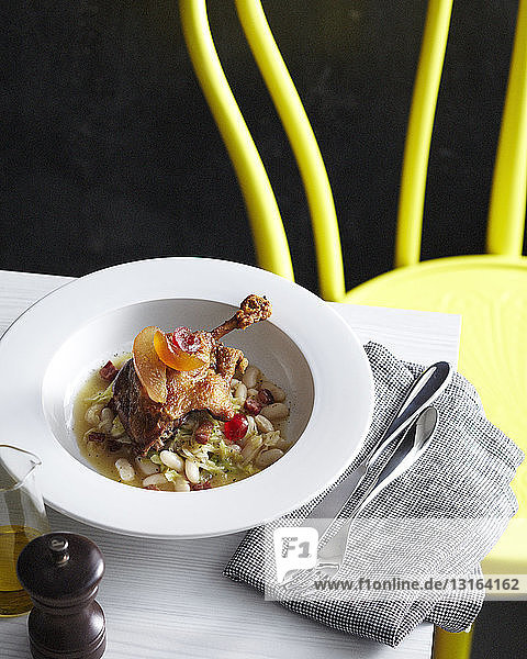 Bowl of duck leg confit with candied fruit garnish served on beans