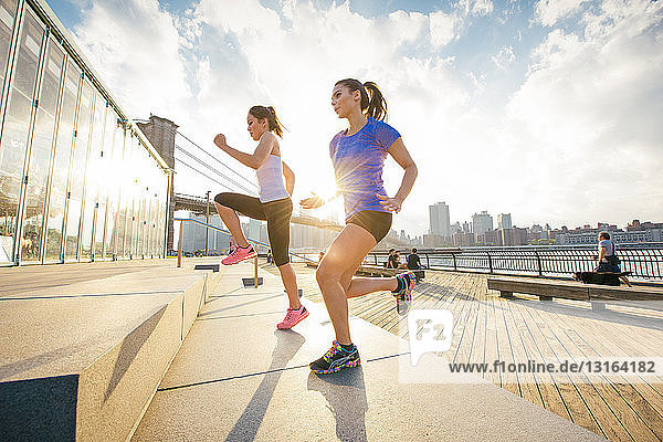 Two female running friends running up stairs on riverside  New York  USA