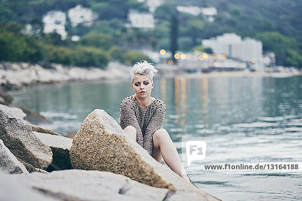 Junge Frau sitzt allein auf Hafenfelsen