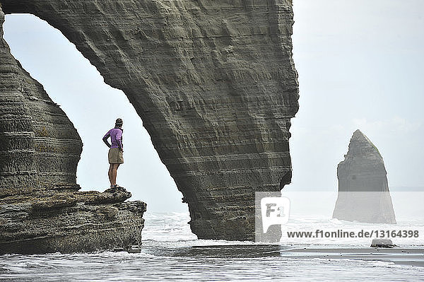 Junge Frau steht auf einer Felsformation am Strand  Nordinsel  Neuseeland