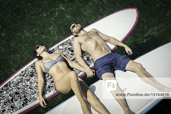 Draufsicht auf ein junges Paar beim Sonnenbaden auf Paddelbrettern