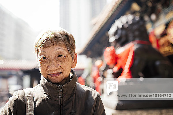 Porträt einer älteren Frau im Mantel vor der Löwenstatue  die in die Kamera schaut