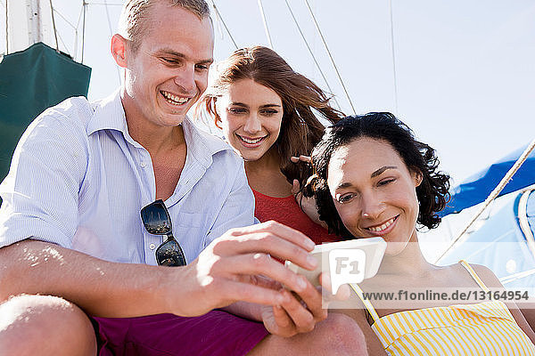 Drei junge Freunde auf einer Yacht mit Smartphone