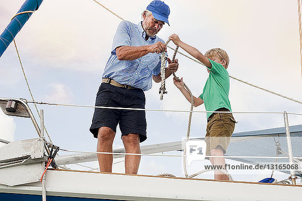 Boy and grandfather knotting rope on sailboat