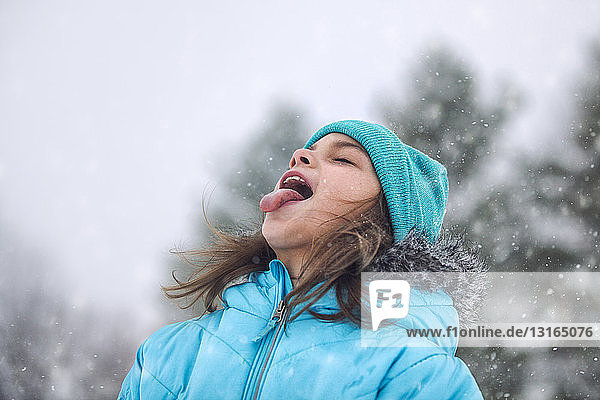 Mädchen schaut auf  streckt die Zunge heraus und fängt Schneeflocken