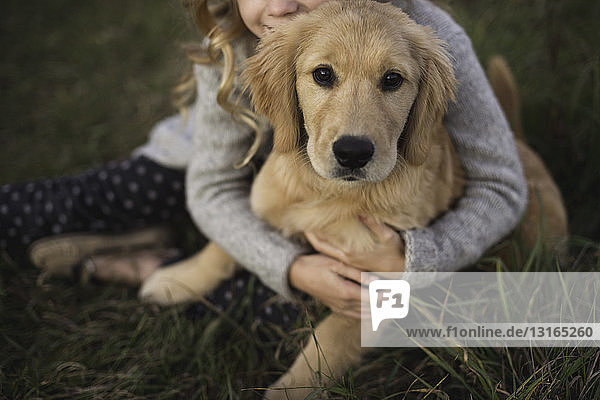 Junges Mädchen sitzt im Gras und umarmt seinen Hund