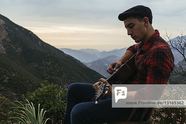 Junger Mann sitzt in Berglandschaft und legt akustische Gitarre  Los Angeles  Kalifornien  USA
