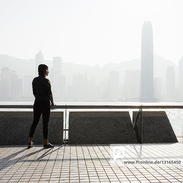 Silhouettierte Seitenansicht einer jungen Frau die über das Wasser auf die Skyline schaut Hongkong China