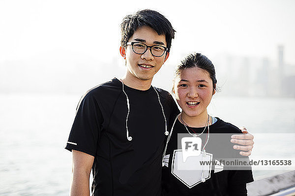 Portrait of young man with arm around young woman  wearing earphones  looking at camera smiling