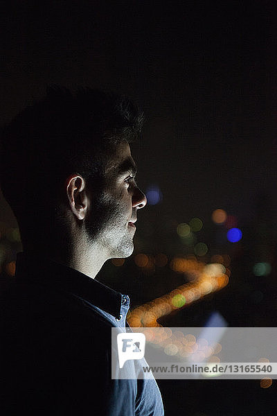 Nahaufnahme eines jungen Geschäftsmannes  der nachts aus dem Fenster eines Bürohochhauses schaut  Shanghai  China