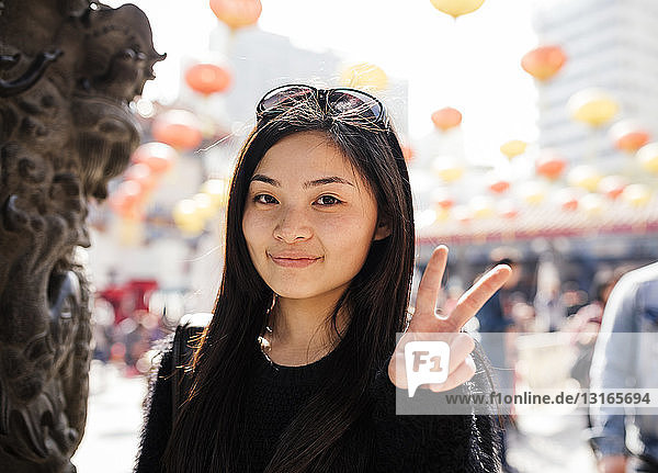 Porträt einer jungen Frau mit langen Haaren und Sonnenbrille auf dem Kopf  die ein Friedenszeichen macht und in die Kamera schaut