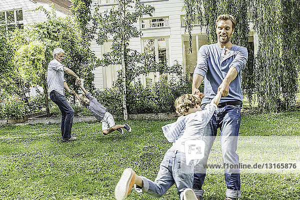 Mittelgroßer erwachsener Mann  dessen Vater mit seinen Söhnen im Garten Schaukeln spielt