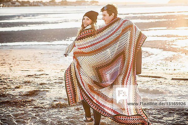 In eine Decke gehülltes Paar spaziert am Strand