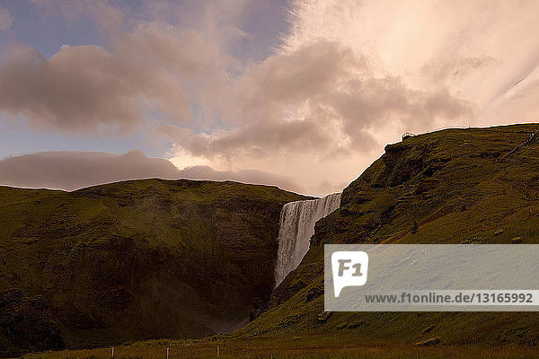 Wasserfall eines Flusses  der bei Sonnenuntergang über eine Bergkette fließt  Island