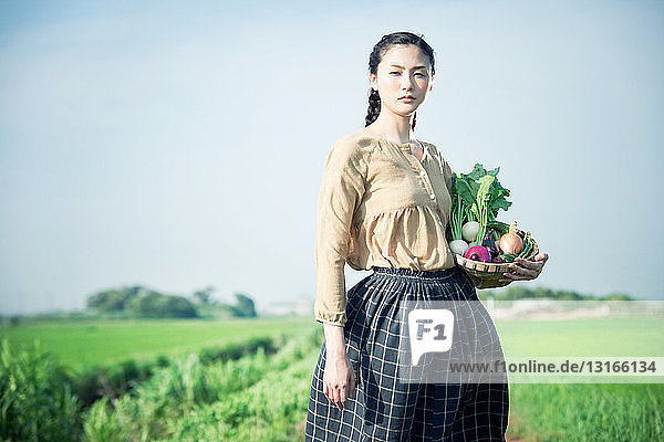 Junge Frau auf dem Feld hält Korb mit selbst angebautem Gemüse