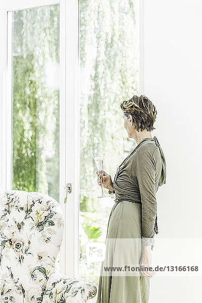 Porträt einer älteren Frau  die im Wohnzimmer aus dem Fenster schaut
