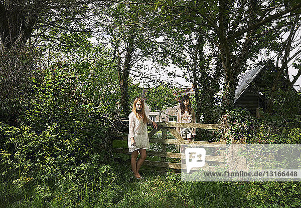 Porträt von zwei jungen Frauen  die vom Feldtor aus starr in die Landschaft blicken